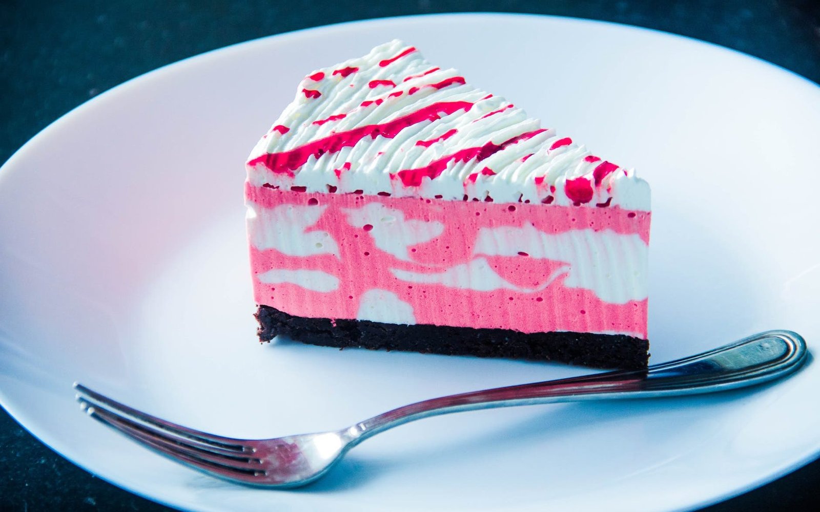sliced white and pink icing covered cake on white plate with silver colored fork